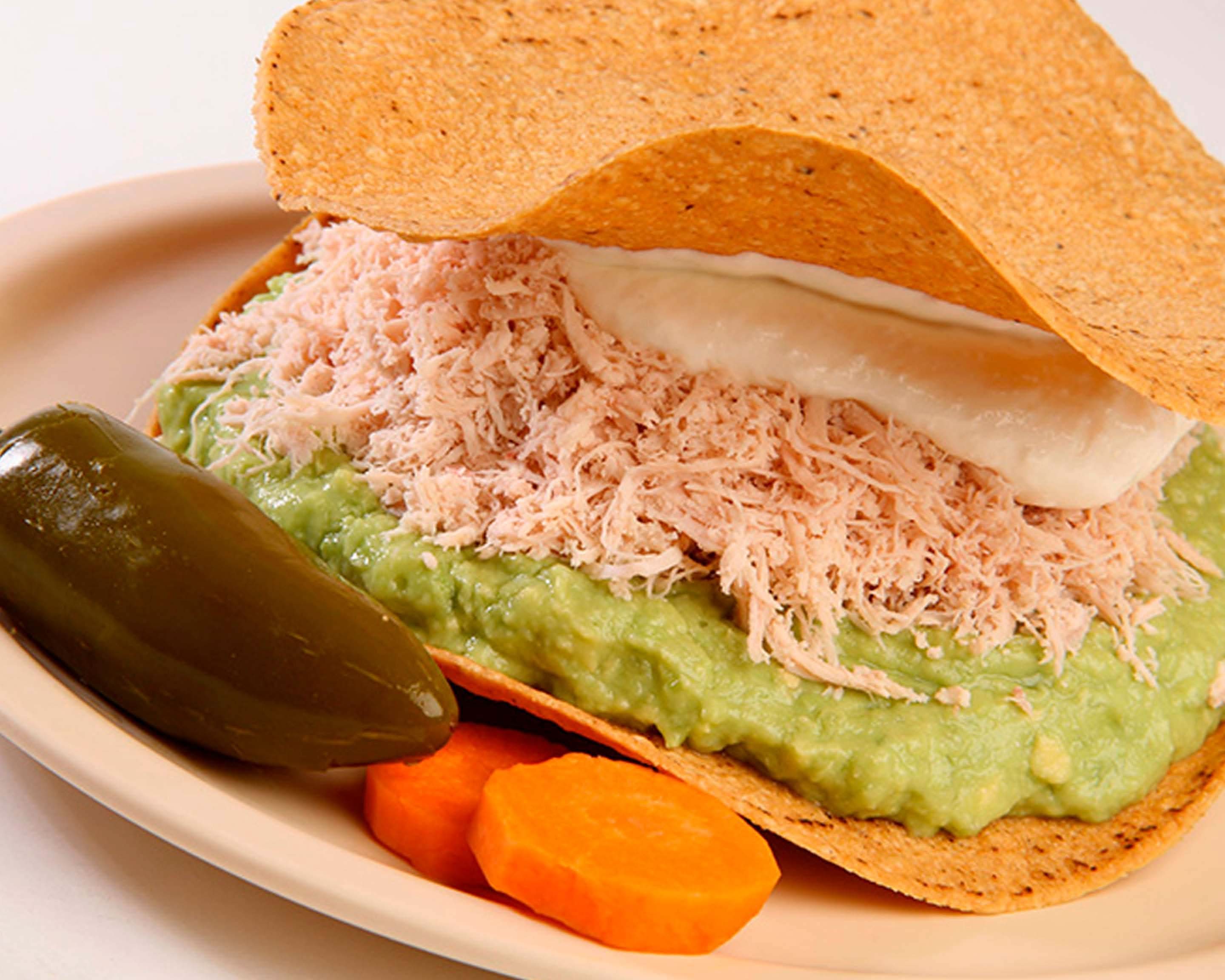 Tuna salad tostada with guacamole, sour cream, and vegetables.