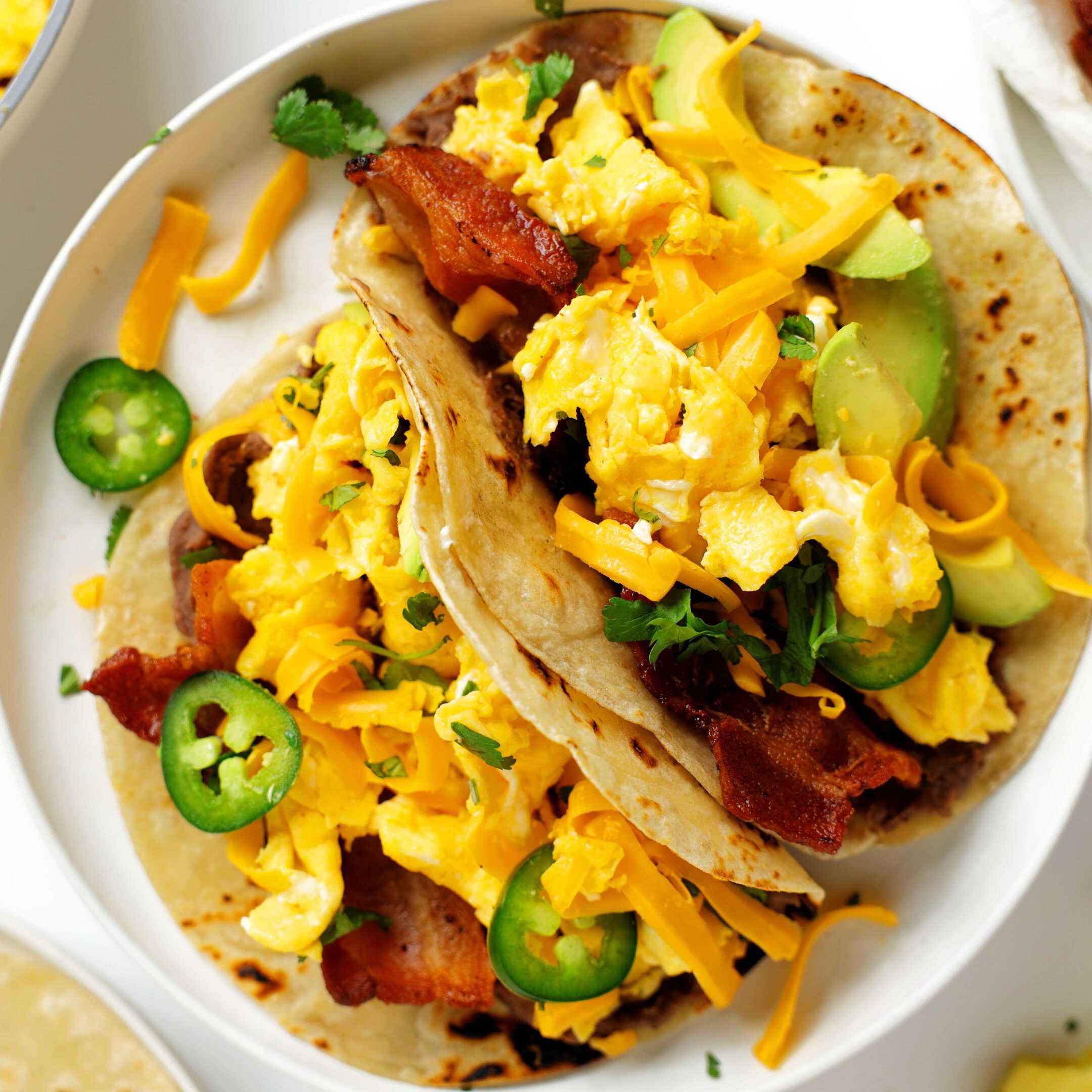 Two breakfast tacos with scrambled eggs, bacon, avocado, and jalapeños.
