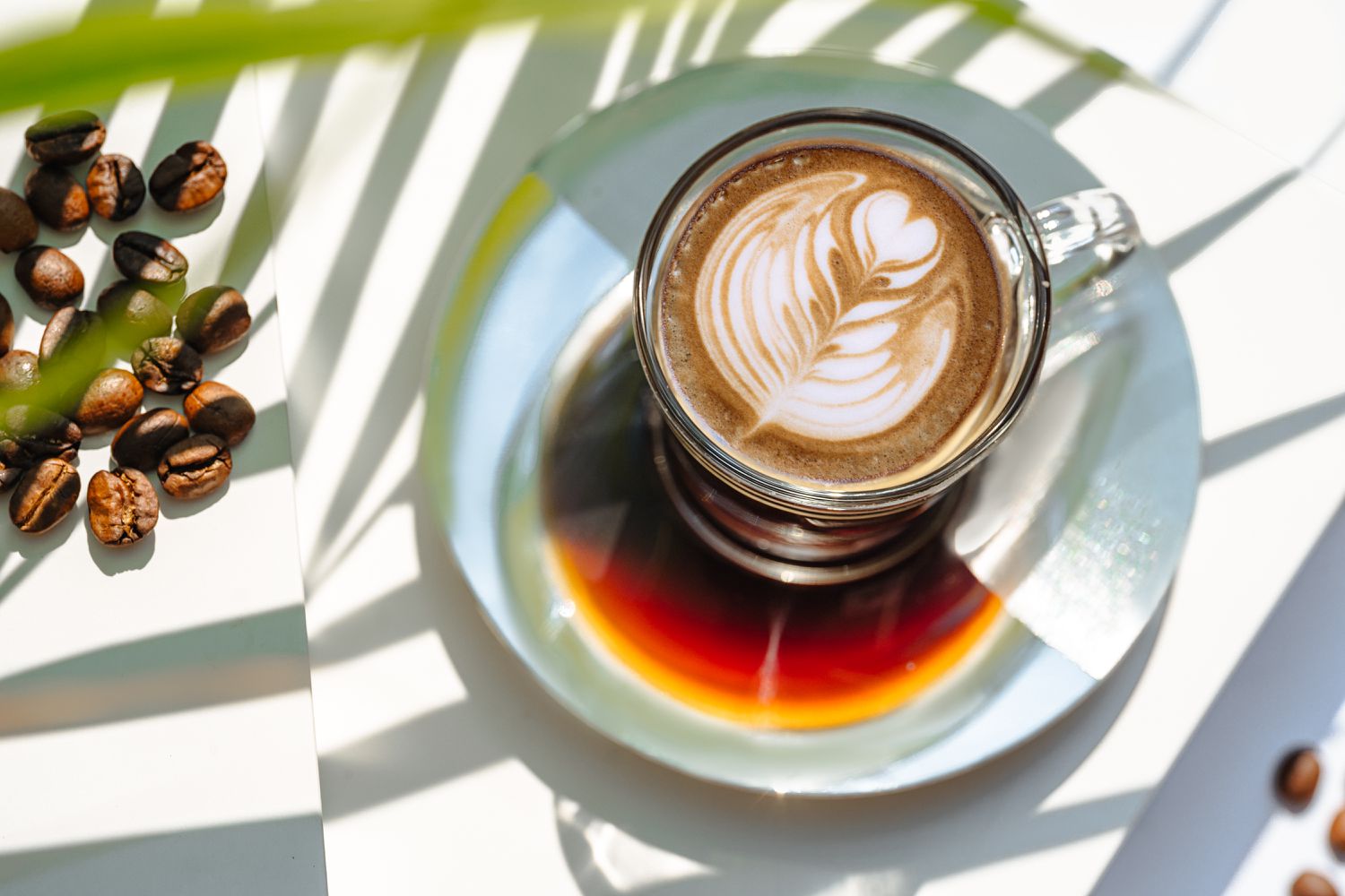 A beautifully crafted latte with latte art in a glass cup on a saucer.